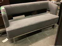 Full view of a gray quilted fabric love seat with chrome legs in worn condition, showing the front and side.