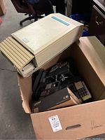 Photo showing a beige Meridian control unit on top of a box filled with black office phones and equipment.