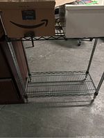 Two-shelf metal wire rack with open wire shelves and vertical supports, showing worn and used surfaces.
