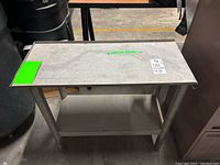 Two-shelf heavy metal table with gray metal surfaces and tubular legs, showing wear