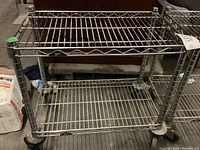 Full view of the Metro two shelf metal wire rolling cart showing the structure, shelves, and wheels.
