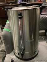 Front and side view of tall stainless steel Nella commercial coffee maker showing water level gauge and metal spout.