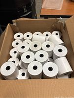 Box filled with multiple white thermal paper rolls with black cores inside a cardboard box.