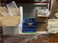 Overview of lot showing rectangular plastic food containers, a blue plastic crate with metal bowls, white buckets, and boxes