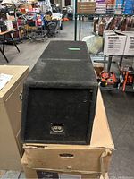 Photo of the side view of a large rectangular speaker cabinet covered in black carpet fabric, showing overall external condition and input connector port.