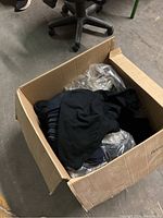 Cardboard box containing folded black T-shirts and some plastic wrapping.