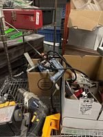 Overview of box with drill, grinder, and clamps on shelf with other boxes and items around.