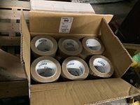 Open cardboard case with six tan tape rolls visible