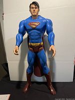 Full front view of large blue Superman action figure with red cape, brown boots and trunks.