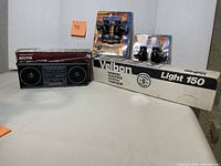 Photo displaying all items in lot: Realistic AM/FM radio in box, Velbon Light Tripod 150 box, two packages of Universal speaker wall mounts.