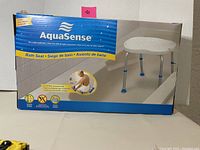 Photo of the AquaSense bath seat in its original packaging showing seat design, brand, and safety features.