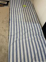 Top view of the blue and white striped mattress on the Coleman camping cot lying flat on the floor.