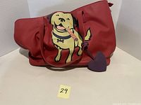 Red tote bag with cartoon yellow dog holding a cigar on front, heart-shaped charm on strap.
