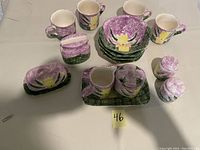 Full view of the set showing mugs, bowls, creamer, sugar container, butter dish, and napkin holder arranged on a table with a lot number card.