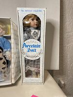 Porcelain doll from The Princess Collection in original box, dressed in a checkered gray and white outfit.
