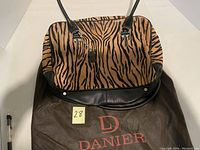 Front view of Danier purse with animal print fabric and leather bottom, resting on a Danier branded dust bag.