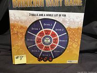 Front view of dartboard game with drinking instructions and three balls visible at bottom, showing condition and design.