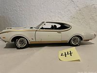 Side view of white and gold 1969 Oldsmobile Cutlass diecast model car showing profile, wheels with Goodyear tires, and body detailing.