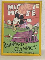 Framed poster showing Mickey Mouse running over a wooden fence with farm animals in a barnyard setting, text includes 'MICKEY MOUSE BARNYARD OLYMPICS A COLUMBIA PICTURE'.