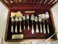 Closed case showing cutlery fitted in burgundy velvet slot interior with label 'Community' on the inside lid and a small cloth piece.