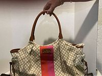 Front view of beige patterned Kate Spade purse with brown leather handles and an orange and pink vertical stripe in the center.