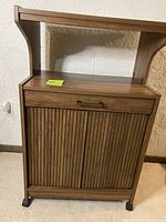 Front view of kitchen stand showing drawer on top, two cabinet doors with vertical slats, and wood grain finish.