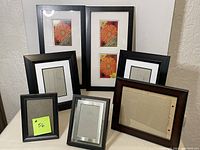 Photo showing 7 assorted picture frames in varying sizes and finishes arranged on a white surface against a wall, including single and double 5x7 frames and an 8x10 frame.