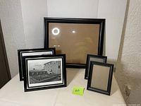Set of 5 picture frames displayed on a white surface against a textured wall. One large 20 x 15.5 inch frame at the back, two medium 8 x 10 inch frames with placeholder images in front left, two small 5 x 5 inch plain black frames on right side.
