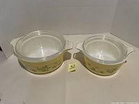 Front view of both Pyrex dishes with lids showing the Shenandoah floral pattern on a yellow band around the exterior, with sized note between them.