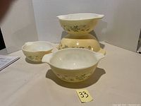 Four vintage Pyrex mixing bowls arranged stacked and then in front, showing Shenandoah green floral pattern over cream base with white interior. Bowls have handles and pouring spouts visible.