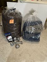 Two sleeping bags in plastic bags along with three dumbbells on carpet floor.