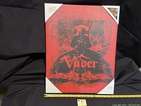 Front view of Darth Vader screen print wall hanging with red and black distressed design in plastic corner protectors.