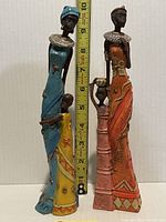 Front view of three African female statues holding children, next to a ruler showing height of about 7 to 8 inches
