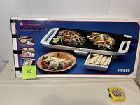 The original box of the Toastmaster Cooledge Grill showing the grill with food on it and the warming tray beneath. Box is intact with graphics and branding visible.