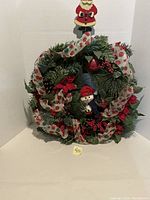 Front view of Christmas wreath with visible snowman figurine, red poinsettias, berries, pine cones, and polka dot ribbon. Wooden Santa hanger at top.