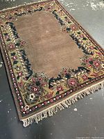 Full view of the handmade wool rug showing the overall floral border design and central plain beige area with fringed edges.