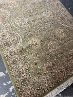 Angled view of one end of the handmade carpet showing green field, floral motifs and border