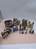 Wide view of entire bisque ceramic Christmas village set showing multiple buildings and figurines arranged together on a light surface.