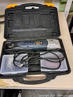 Closed and open black plastic carrying case containing the multifunction tool with power cord and accessory boxes