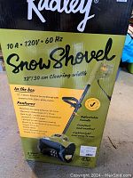 Box showing Radley brand and features of the electric snow shovel including 12 inch clearing width, 10A 120V 60Hz motor, maximum throwing distance 20 feet, maximum intake height 6 inches, built tough for impact and low temperature, LED light for nighttime use, paddle auger, up to 2500 RPM, weight 13 lb 2 oz, 3 year limited warranty.