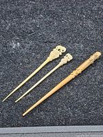 Three hair pins shown on a black textured surface, two bone pins with elephant toppers and one wooden carved pin