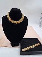 Close-up of the chunky vintage heavy gold tone necklace on black bust, showing detailed linked overlapping leaf or scale pattern and rhinestones.