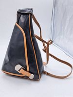 Side view of black leather handbag with tan leather trim and unique silver-tone clasp.