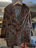 Full view of the brown vintage ladies' fur coat hanging on a hanger, showing front and collar.