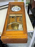 Full frontal view of the vintage oak pendulum wall clock showing wooden case, glass panels, clock face, and pendulum.