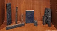 Photo of nine assorted Asian wooden printing blocks with carved characters and script arranged in groups on wooden shelf.