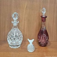 Set of three vintage glass bottles: heavy clear crystal liquor decanter, ruby red glass decanter, and small perfume bottle with bird stopper.
