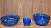 Full set of six Pyrex cobalt blue ribbed glass bowls and casserole dish arranged side by side on a wooden surface.
