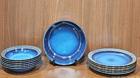 Image showing 6 pasta bowls stacked, one pasta bowl on stand, and 6 plates stacked, all with blue gradient and textured rim pattern.