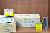 Commercial heavy-duty stapler with black handle next to three boxes of yellow Arrow Fastener staples 1/2 inch size, and several cardboard boxes including Symaskine Motor and fan kit.